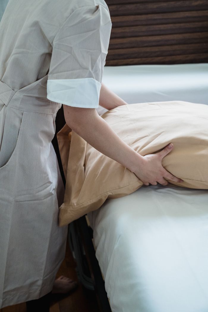 Home Hotel staff adjusting a pillow on a bed, ensuring guest comfort in a cozy room.