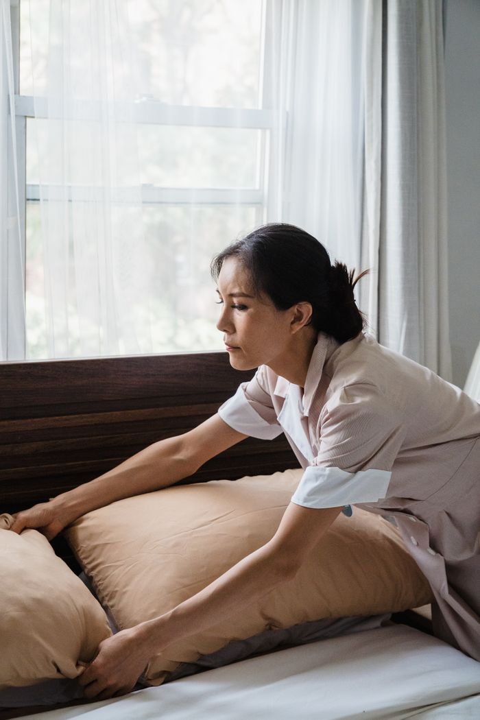 A dedicated housekeeper tidying a hotel bed, enhancing room comfort.